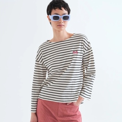 Pessoa com óculos de sol azuis, camisa às riscas pretas e brancas com cão rosa e calças de veludo cotelê rosa