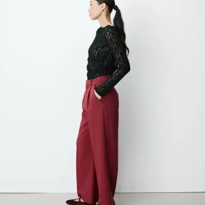 Mulher de perfil com blusa preta de renda e calças vermelhas