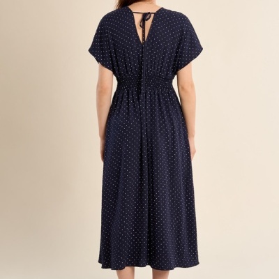 Vestido midi azul escuro às pintas brancas visto de costas com laço e sandálias