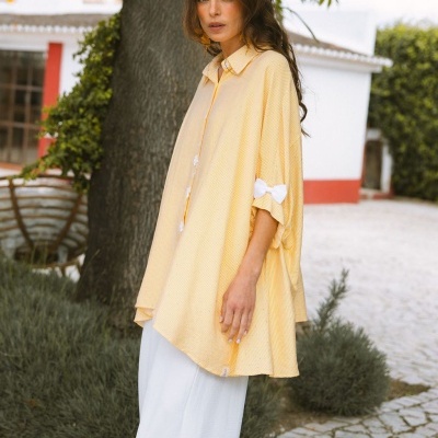 Blusa amarela clara de riscas finas com laço branco na manga e calças largas brancas ao ar livre