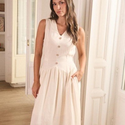 Vestido feminino comprido claro com botões, sem mangas, apresentado por mulher em ambiente interior branco.