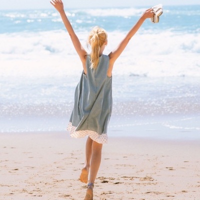 Criança com vestido na praia segurando sandálias