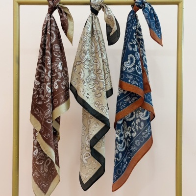Três lenços com padrão paisley pendurados num suporte amarelo.