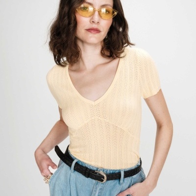 Mulher com camisola bege, calças de ganga e óculos amarelos