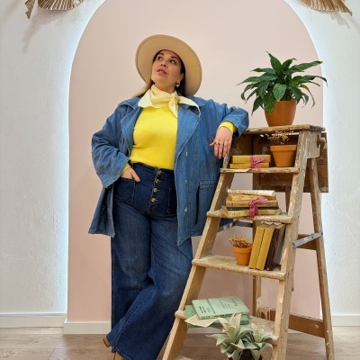 Mulher com fato de ganga e camisola amarela junto a escada de madeira com plantas e livros