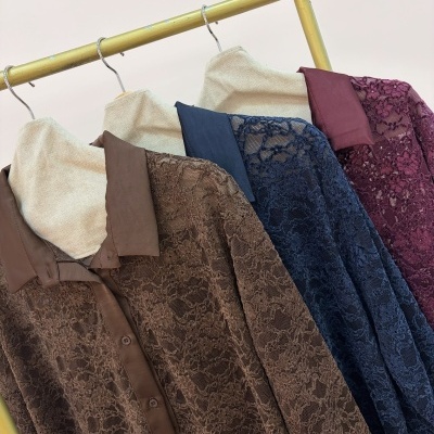 Três camisas de renda castanha, azul escuro e vinho penduradas num tubo metálico amarelo.