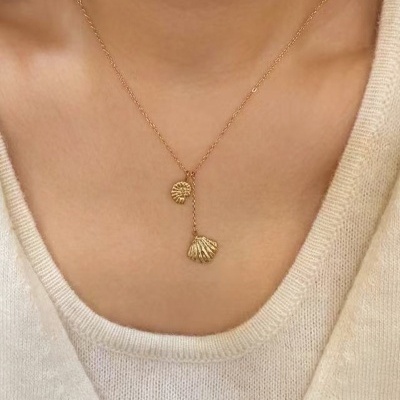 Colar dourado com pendentes de conchas em pescoço de pessoa com camisola branca