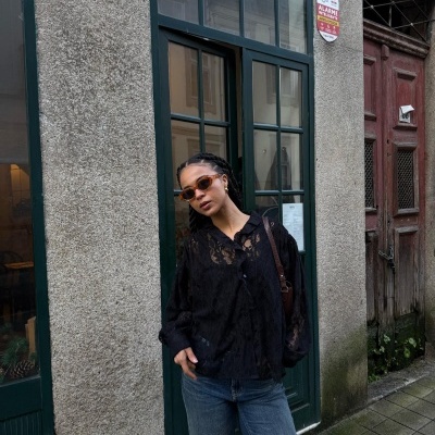 Mulher com blusa preta de renda, calças de ganga e óculos de sol