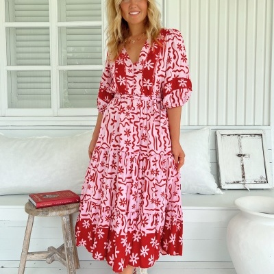 Vestido midi vermelho e rosa com padrão floral e abstrato, manga 3/4, cinto fino, tecido fluido, usado com ténis brancos, em cenário interior branco com janela e mobília rústica