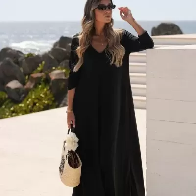 Mulher com vestido preto longo e mala de palha junto ao mar