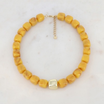 Colar de contas amarelas quadradas com uma conta dourada no centro e fecho dourado sobre fundo branco.
