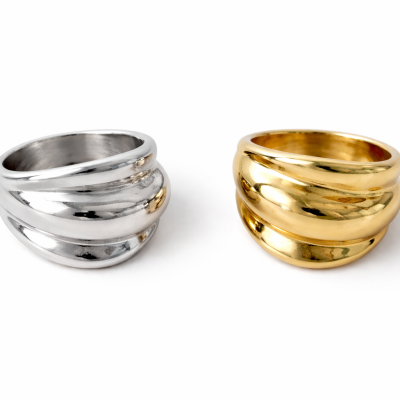 Dois anéis largos, um prateado e outro dourado, com design ondulado