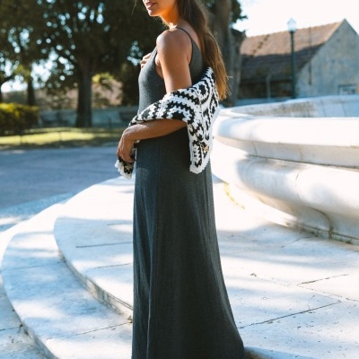 Mulher com vestido longo castanho escuro e cardigan preto e branco ao ombro em escadaria exterior