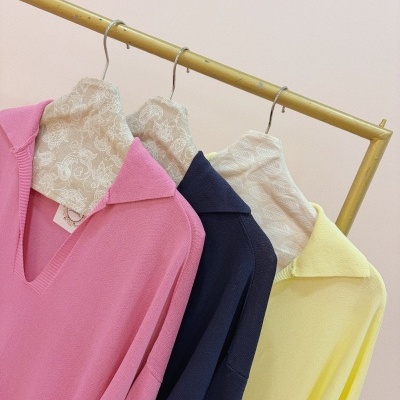 Camisolas de malha rosa, azul escuro e amarelo penduradas em cabides decorativos num suporte amarelo