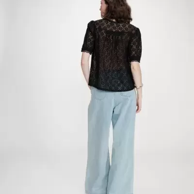 Mulher de costas com blusa preta em renda e calças de ganga azul clara