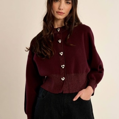 Cardigan bordeaux com botões de coração e calças pretas numa modelo.