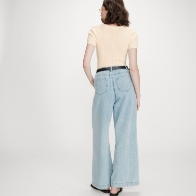 Mulher de costas com camisola bege, jeans largos azuis e cinto preto