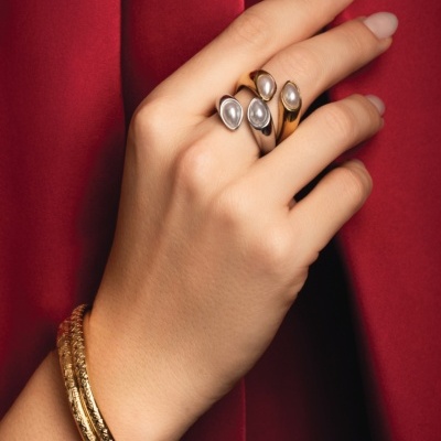 Mão com anéis de pérola e pulseiras douradas em fundo vermelho