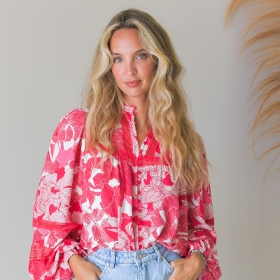 Mulher com blusa floral vermelha e branca e calças de ganga azuis.