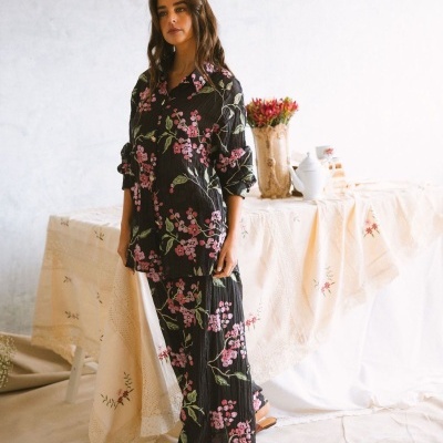 Conjunto de camisa e calças florais negras com padrão rosa e verde em ambiente interior