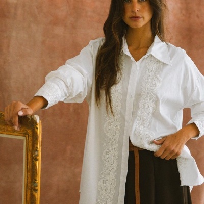 Mulher com camisa branca bordada, saia preta e fita de cabelo preta com flores brancas