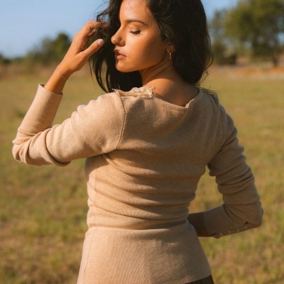 Mulher de cabelos castanhos escuros com camisola bege de malha e saia castanha num campo aberto