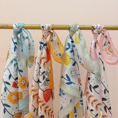 Quatro lenços florais coloridos pendurados numa barra amarela.
