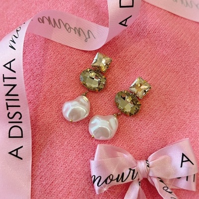 Brincos com pedras douradas e pérolas sobre fundo rosa com fita