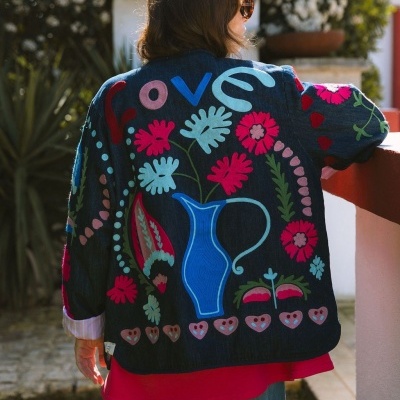 Casaco escuro com estampa colorida floral e jarro azul, usado por mulher de costas ao ar livre