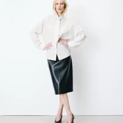 Mulher a usar camisa branca às riscas, saia midi preta com textura e sapatos de salto