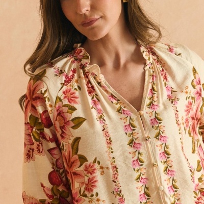 Blusa feminina floral bege com gola franzida e botões, usada por mulher com brincos dourados em formato de coração