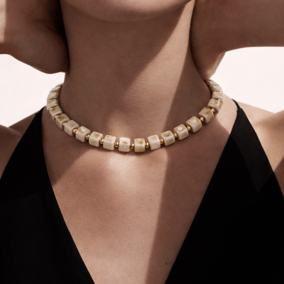 Colar com contas quadradas bege e douradas num pescoço feminino com vestido preto