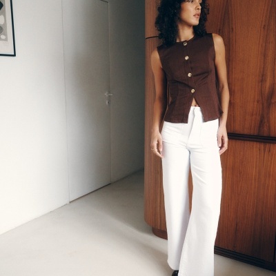 Mulher vestindo top castanho sem mangas com botões dourados e calças brancas largas