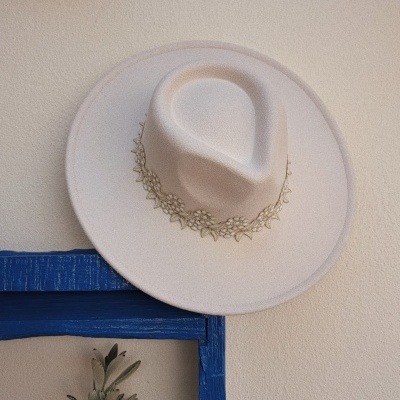 Chapéu bege de feltro com faixa floral bordada pendurado numa parede creme