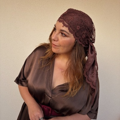 Mulher com lenço castanho em renda e vestido castanho acetinado