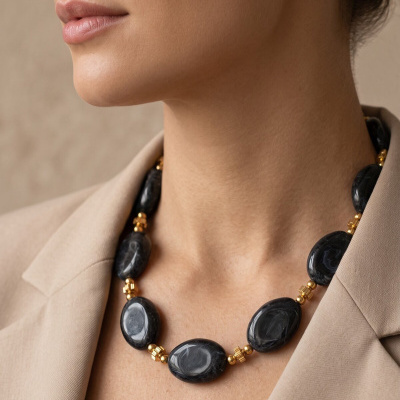 Colar preto com contas douradas no pescoço de mulher com blazer bege