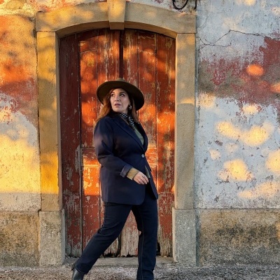 Mulher de blazer azul e chapéu verde em frente a porta de madeira vermelha envelhecida