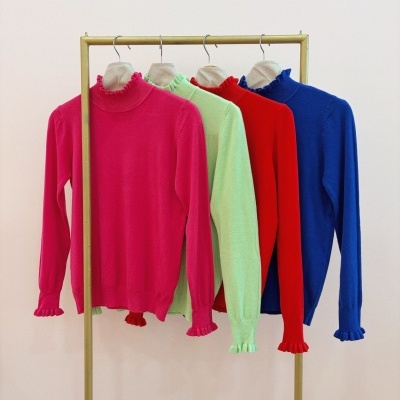 Camisolas de malha coloridas com gola e punhos frisados penduradas num cabide.