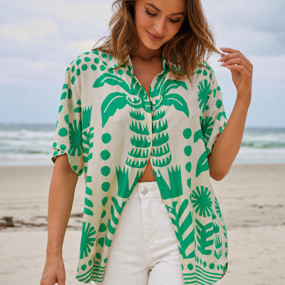 Modelo usando camisa bege com padrão verde e calças brancas na praia