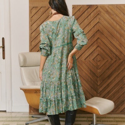 Vestido comprido verde com padrão floral e paisley em ambiente interior com cadeiras de escritório e painéis de madeira