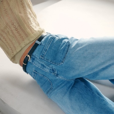 Jeans azul claro com cinto preto e top bege texturizado.