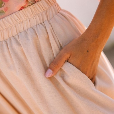 Saia bege com cintura elástica e bolso, com mão numa das dobras, e blusa floral rosa