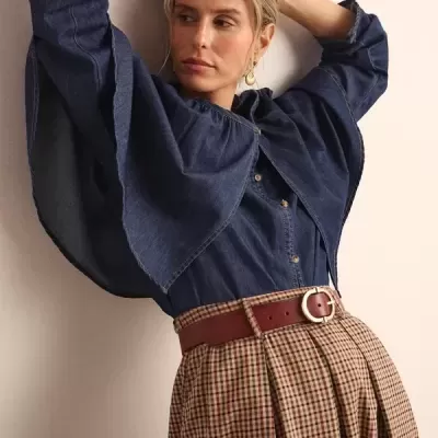 Mulher com camisa de ganga azul e saia xadrez às pregas com cinto castanho