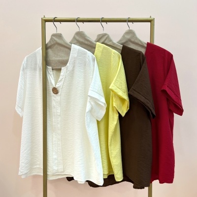 Blusas de manga curta branca, amarela, castanho e vermelha penduradas em cabides com capa bege em cabide metálico