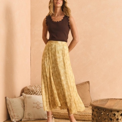 mulher com blusa castanha e saia amarela em ambiente interior com almofadas e mesa de madeira