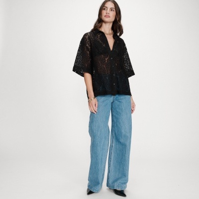 Camisa preta de renda feminina com calças de ganga azuis e sapatos pretos em fundo branco