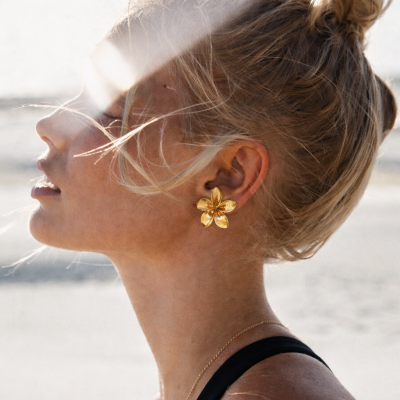 Mulher usando brinco dourado em forma de flor e colar dourado