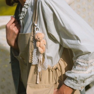 Mochila bege com chaveiro ursinho em pelúcia e camisa branca com detalhes em renda