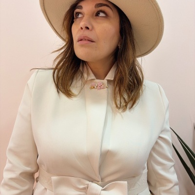 Mulher com jaqueta branca com laço grande na cintura e chapéu bege