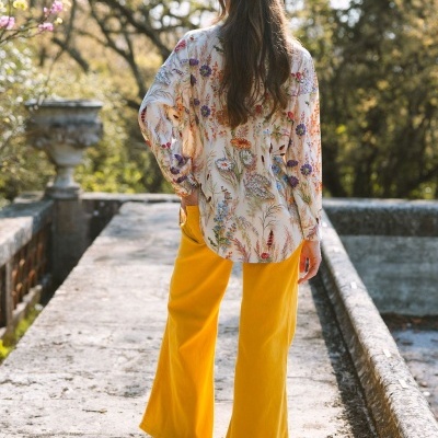 Pessoa com camisa estampada floral e calças amarelas largas vista de costas ao ar livre